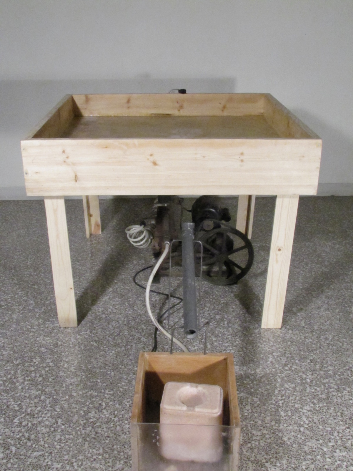 Wooden water table with a pump mechanism and a clear box holding a pale cast form.