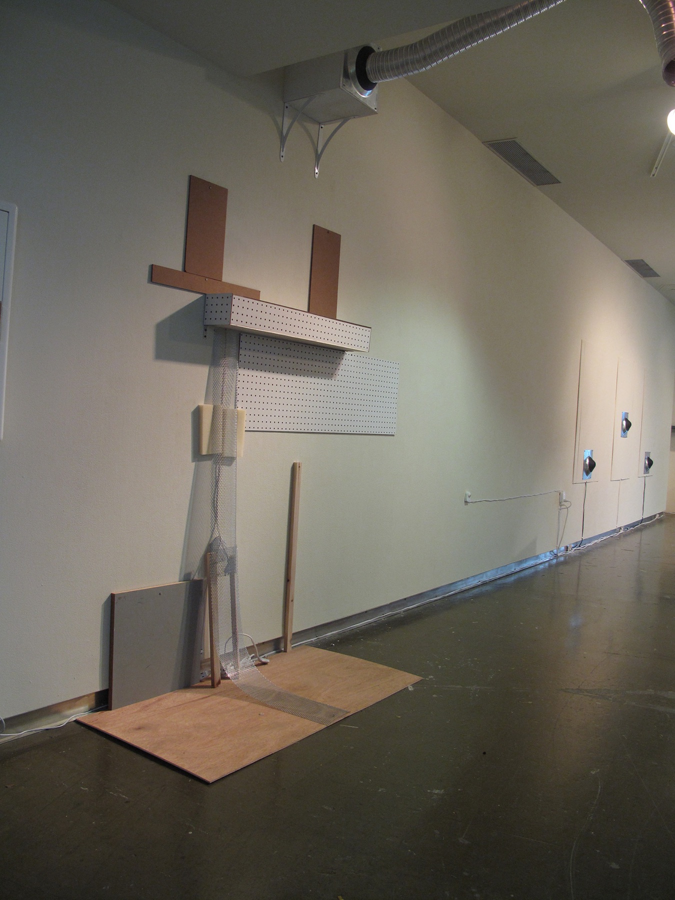 Gallery corridor lined with perforated panels, wood strips, wall-mounted components, floor elements, and visible cabling.