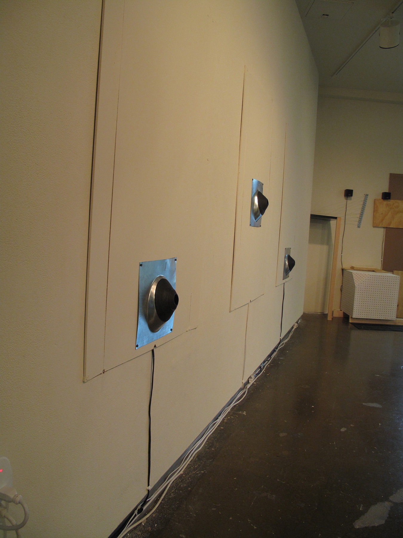 Gallery wall with circular black components mounted on blue square plates and connected by visible cables.