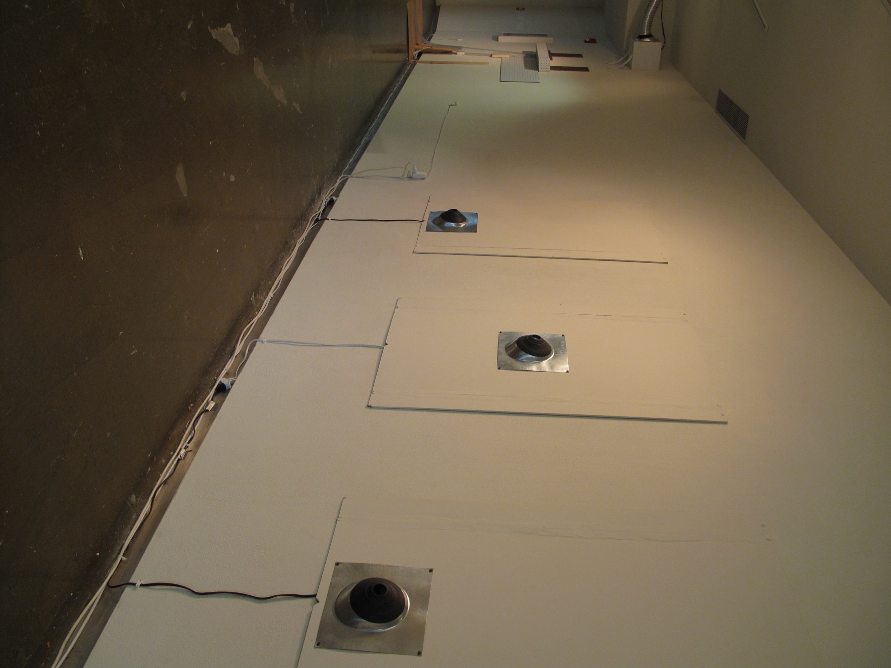 Three circular black components mounted along a gallery wall on square plates with visible connecting cable.