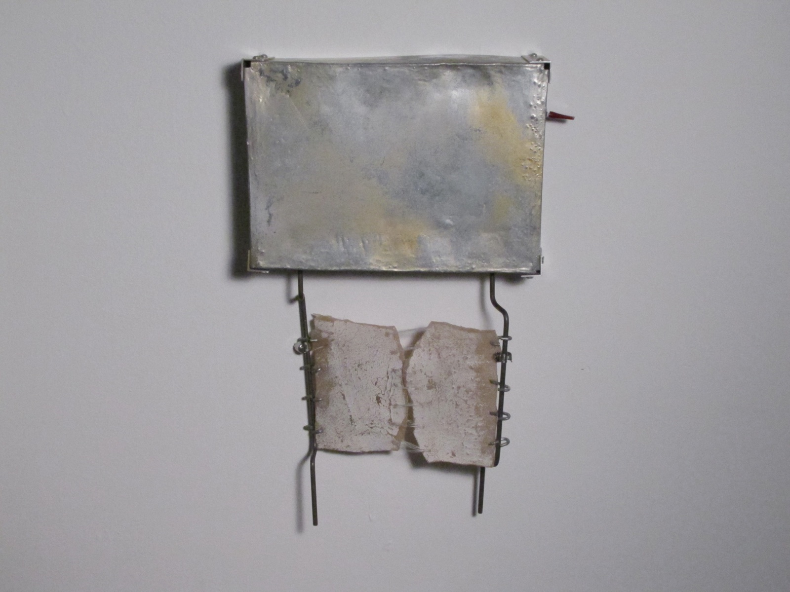 Wall-mounted steel apparatus holding two pale cast polyurethane forms between narrow metal rods.