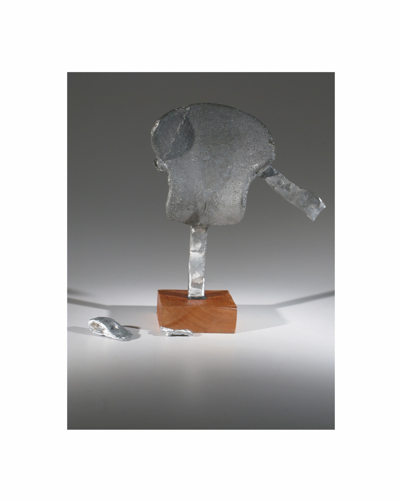 Cast aluminum form with a rounded gray body and projecting fragments mounted on a small wood base.