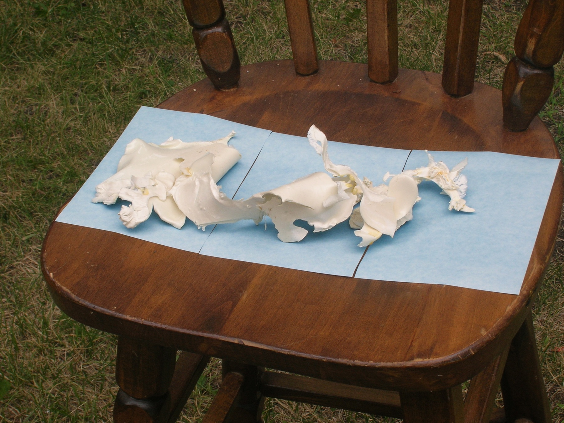Irregular white cast-plastic forms spread across blue paper on a wooden chair outdoors.