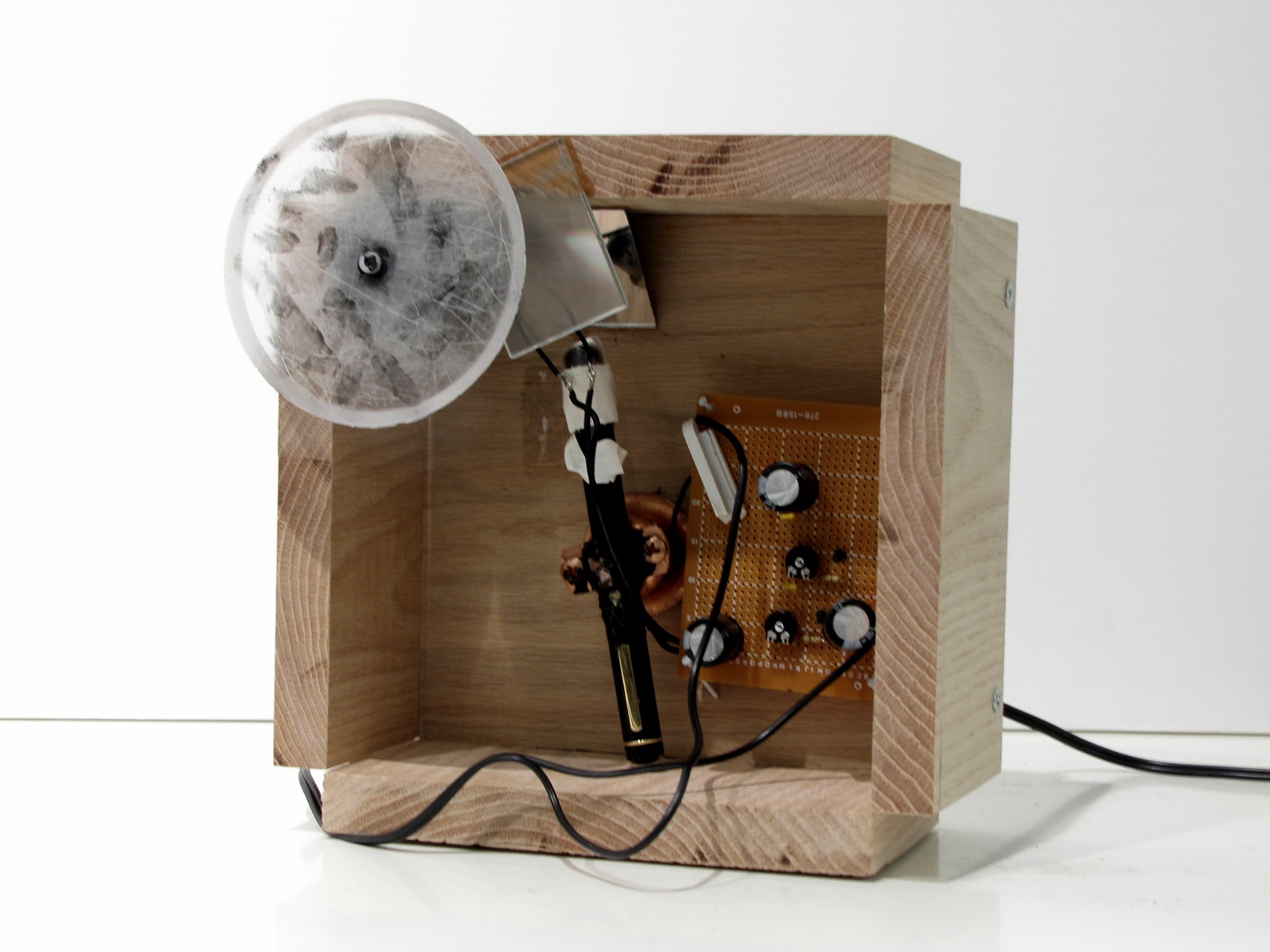 Wood enclosure holding a small circuit board, wires, a mirror, and a translucent circular lens.
