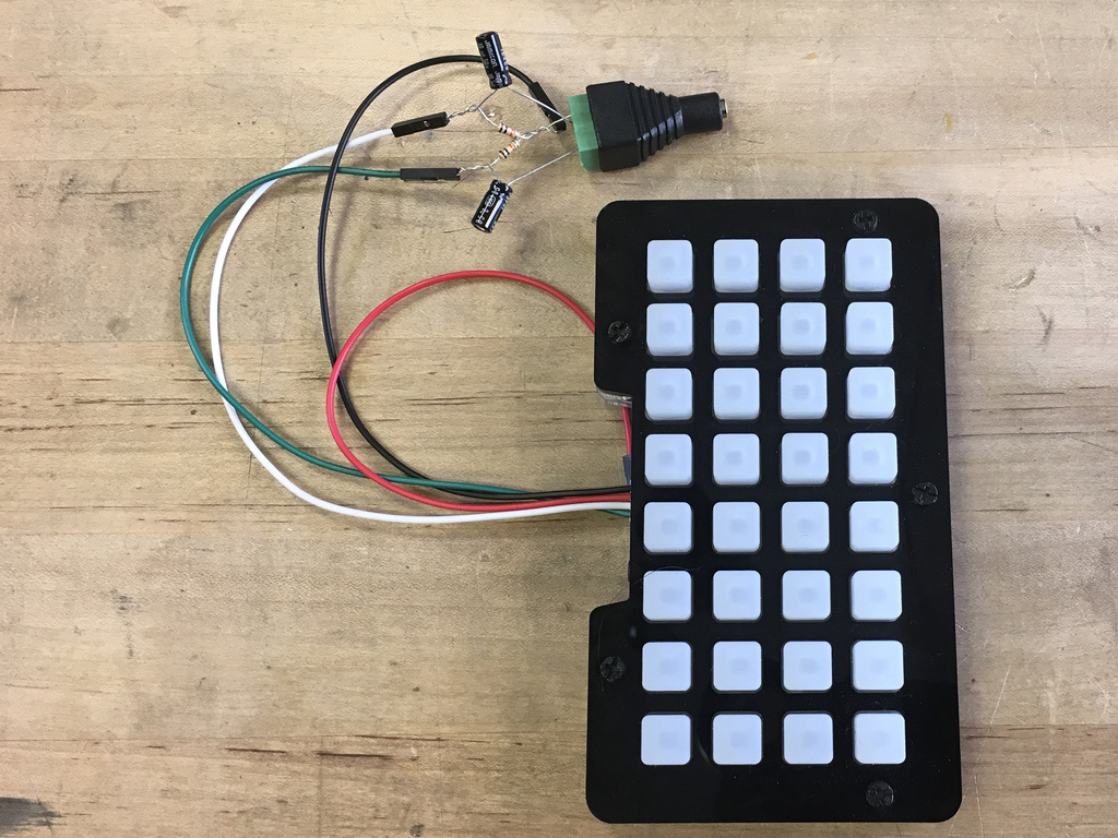 Black NeoTrellis sampler with a four-by-eight grid of white pads, exposed audio components, and colored wires on a wood workbench